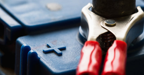 A close-up of a battery with black casing and a charger with a red handle on the post with wires coming off of it.