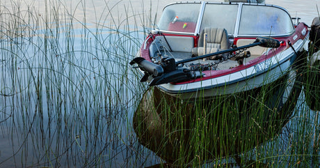 A red fishing boat anchored in the reeds with a trolling motor attached to the front, ready to be deployed.