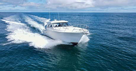 A white yacht sailing on the water during the day beneath white clouds and a blue sky with a long line of wake behind it.