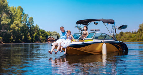 A dad and his daughter sitting on the bow of a boat. The mother of the family is slowing driving the boat through the water.