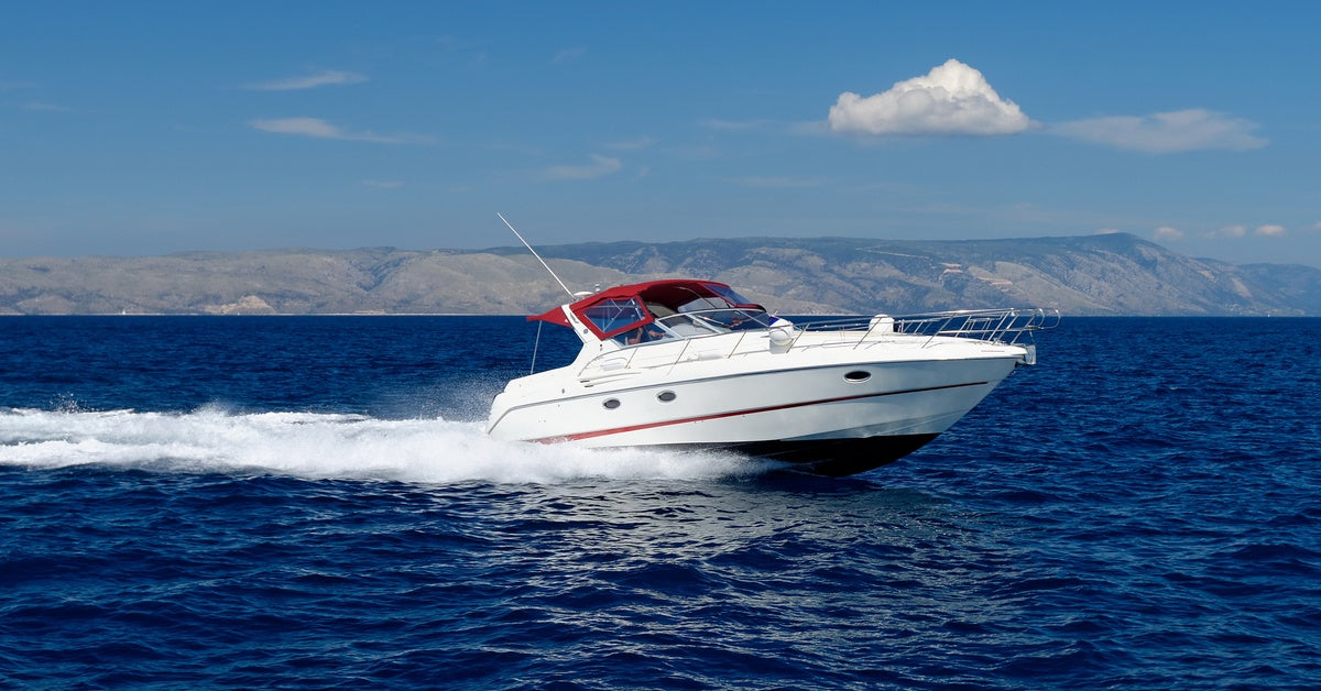 A white boat with a red roof cruising on the water during the day with mountains and a blue sky in the background.