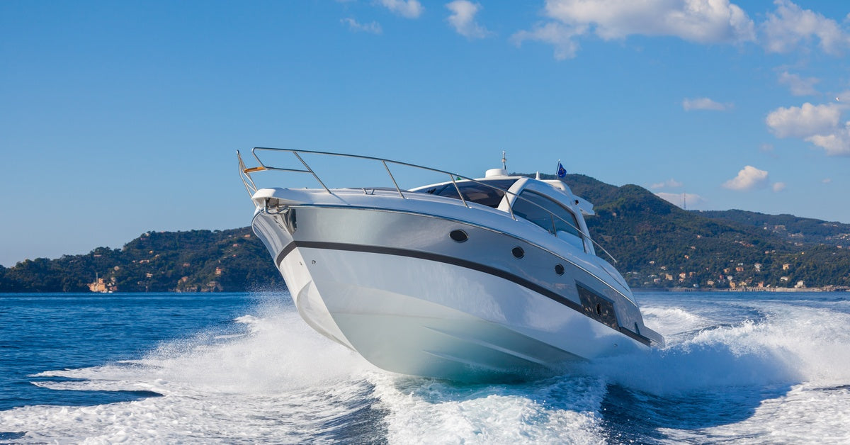 A motorboat riding over white choppy waves on the water with a large hill in the background beneath a blue sky.