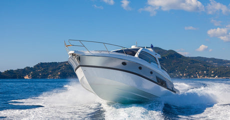 A motorboat riding over white choppy waves on the water with a large hill in the background beneath a blue sky.