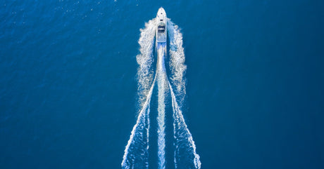 An overhead view of a white motorboat moving over the blue water during the day as it creates wake behind it.