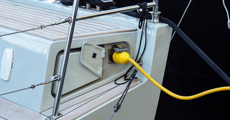The back end of a boat featuring a battery charging port. A large yellow cable is plugged into the port to charge the battery.