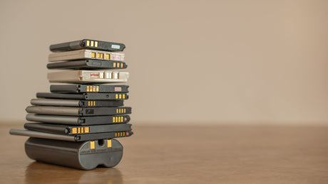 A stack of lithium batteries for different types of devices sitting on a wood floor with a white background.