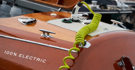 A red boat with 100% ELECTRIC written on it sitting in a marina. There’s a yellow charging cable plugged into it.