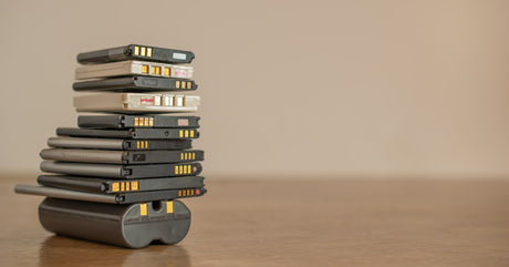 A group of lithium-ion battery cells stacked on top of one another on a wood floor with a white wall in the background.