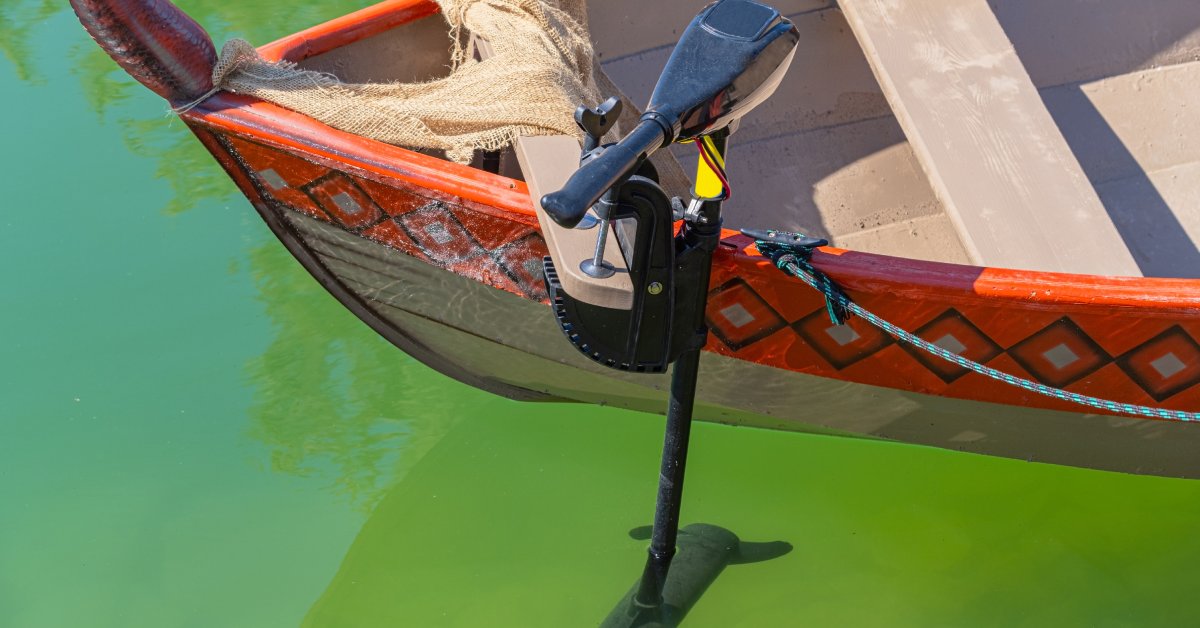 A small wooden boat that has intricate designs painted on it has a trolling motor attached to the back.