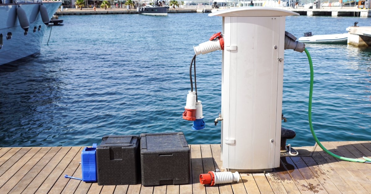 A white battery charging station sitting on a dock in a marina next to a couple of battery cells in black containers.