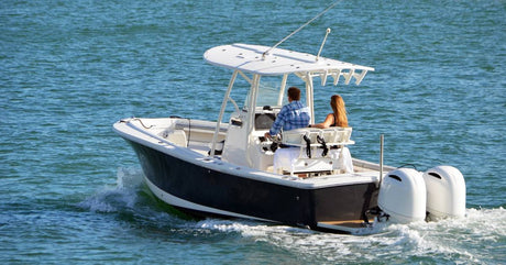 A boat on the water with two motors attached to the back and a couple standing beneath an awning while operating it.