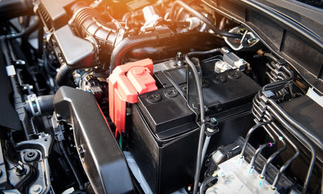 An automotive battery is sitting in a vehicle’s engine bay. All of the engine components are clean.