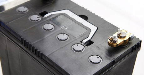 A close-up of a battery in a black case with a silver handle and two clean metal posts on either side of the top.