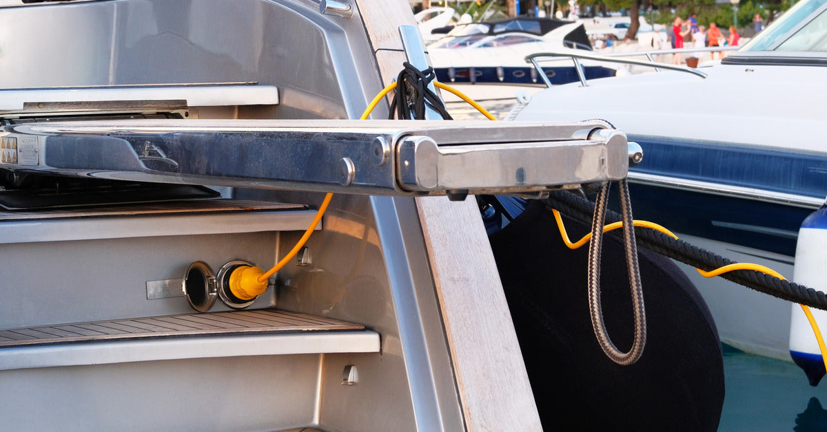 A small boat parked at a dock. The boat is plugged into an electrical outlet from a charging station.