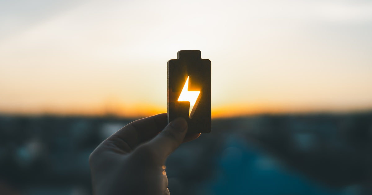 A person holding up a wooden block in the shape of a battery. Light passes through negative space in the block to reveal a bolt.