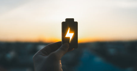 A person holding up a wooden block in the shape of a battery. Light passes through negative space in the block to reveal a bolt.