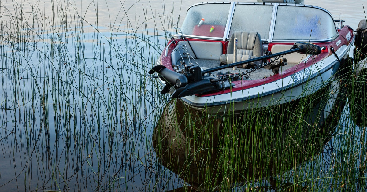 A red-and-white boat with a trolling motor lifted out of the water. The boat is currently tied up and still.