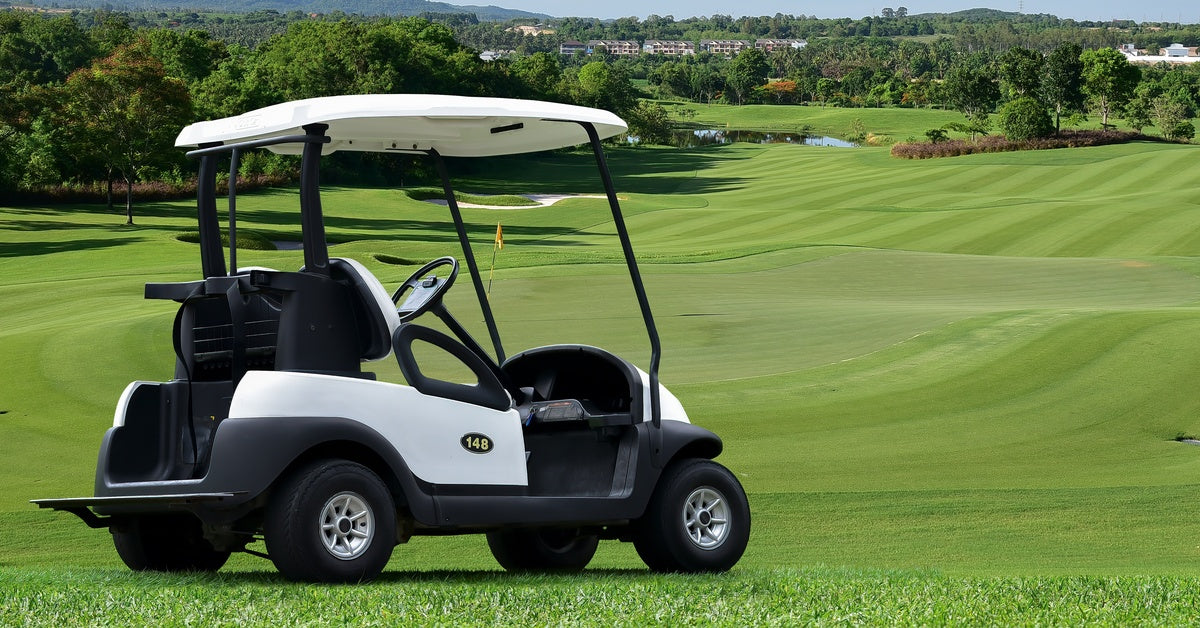 A parked black-and-white golf cart sitting on a golf course, with rolling course fields expanding before it.