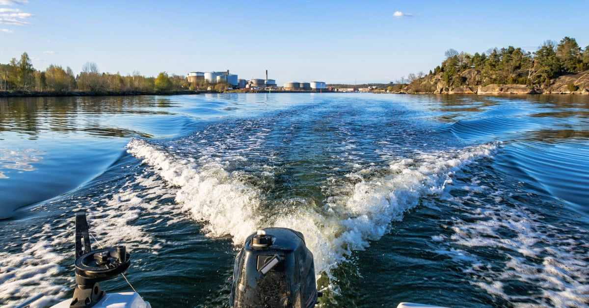 A small motorboat traveling through a wide river. The boat's trolling motor is creating white ripples in the water.