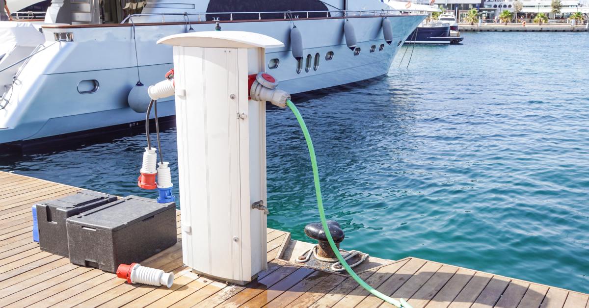 A charging cable connected to a charging port on a boat dock. There are black marine batteries sitting beside it.
