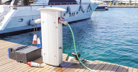 A charging cable connected to a charging port on a boat dock. There are black marine batteries sitting beside it.