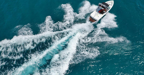 A small white boat with a black roof speeding through open teal-blue water and leaving a wide wake behind it.