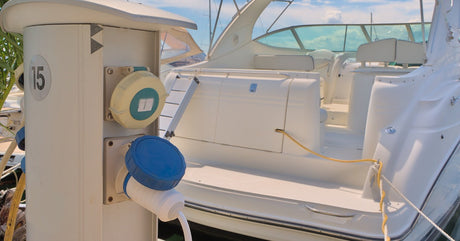 A boat docked on a sunny day. The boat's yellow cord stretches out to connect to the dock's electrical charging port.