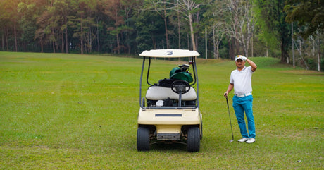A golfer standing beside a still golf cart and holding their hand up to their head to convey a stressed or upset mood.